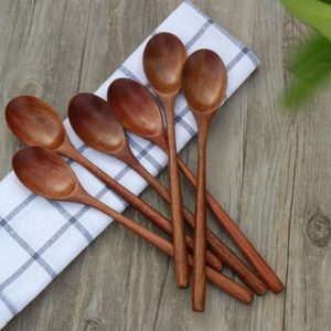 Wooden spoons lie on a checkered cloth, placed on a wooden surface with green leaves visible in the corner.