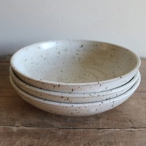 Ceramic bowls stack neatly on a rustic wooden table, showcasing their speckled design against a plain background.