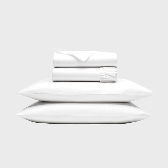 White bed sheets and pillowcases neatly stacked; pillows beneath, sheets rolled on top, against a plain gray background.