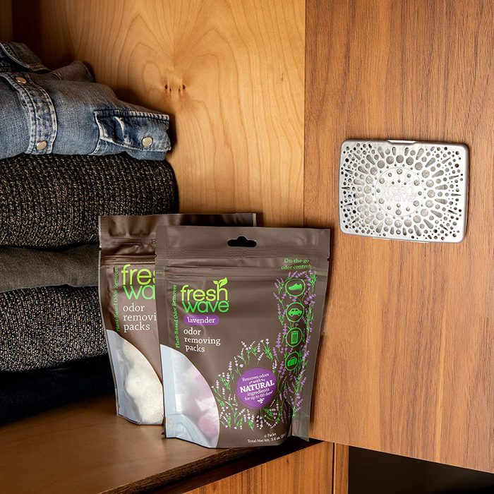 Odor removing packs sit in a wooden cabinet near folded clothes, next to a perforated metal scent diffuser.