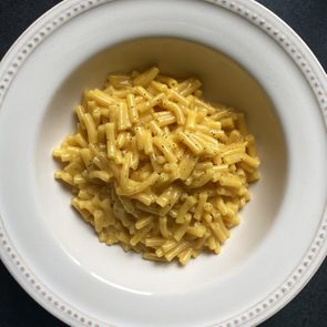 A plate holds creamy macaroni and cheese, sprinkled with black pepper, placed on a dark surface.
