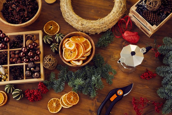 High angle view of beautiful toys and fir tree twigs for making Christmas wreath placed on wooden table with secateurs and coffeemaker