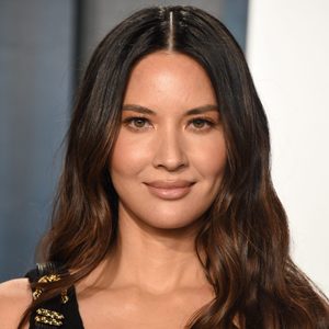Person smiling subtly, gazing forward; long, dark hair; indoor setting with neutral background.