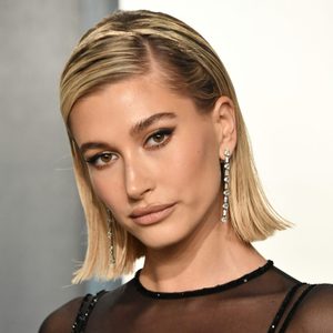 Person gazes confidently, wearing elegant long earrings, in a well-lit setting with a neutral background.