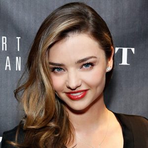 A person smiling confidently, standing in front of a dark backdrop with partially visible text.