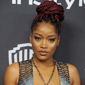 A person with braided hair poses confidently against a dark backdrop with partially visible text and logo.