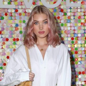 A person stands against a colorful sequin backdrop, wearing a white shirt, holding a beige bag. Text 