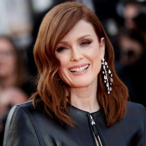 Person smiling, wearing diamond earrings and a leather jacket, in a blurred crowd setting.