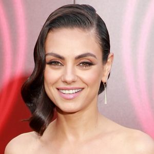 A person smiles warmly, showcasing earrings, against a soft-focus background with pinkish hues.