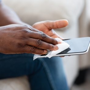 Hands wipe smartphone; seated person in casual jeans.