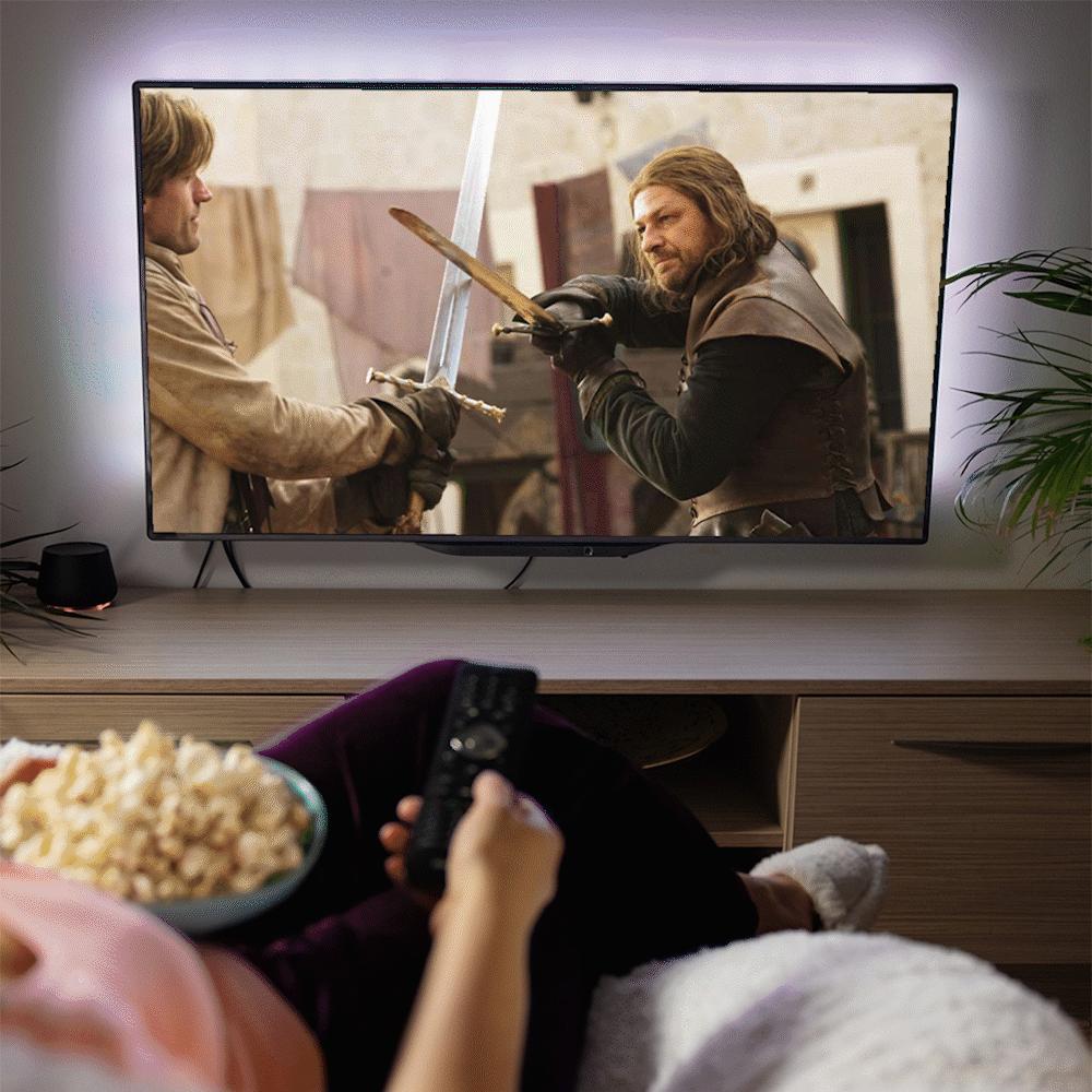 Person holds remote, eating popcorn, while watching sword fight scene on TV; cozy living room setting with plants and soft lighting.