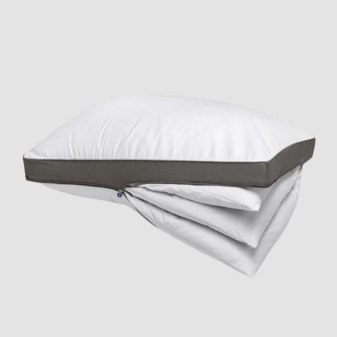 White pillow with a zippered side, displaying layered inserts, set against a plain gray background.