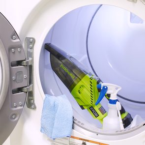 Vacuum, cloth, spray bottle sit inside open washing machine, showcasing cleaning tools in storage.