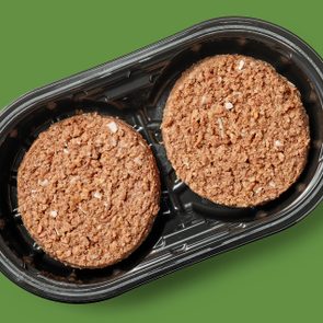 Two brown, textured patties sit in a black plastic tray on a green background.