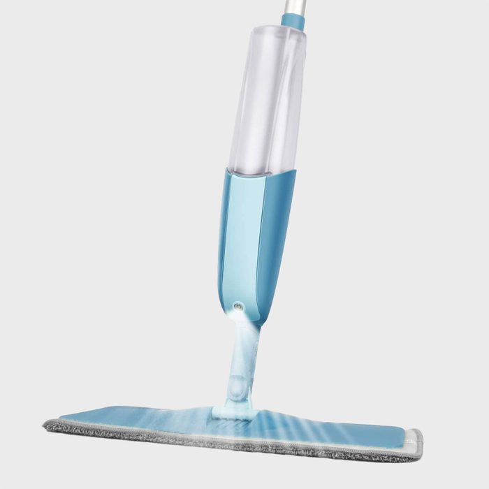 A blue spray mop dispenses liquid onto the flat cleaning pad, set against a plain white background.