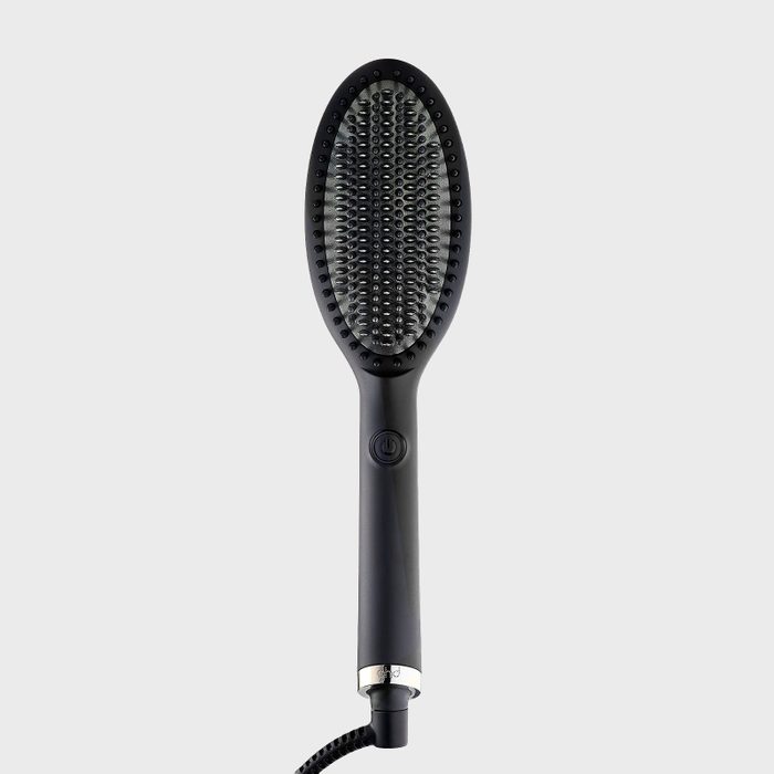Hairbrush lies upright; bristles arranged symmetrically; sleek, black handle with power button; coiled cord attached; plain light gray background.