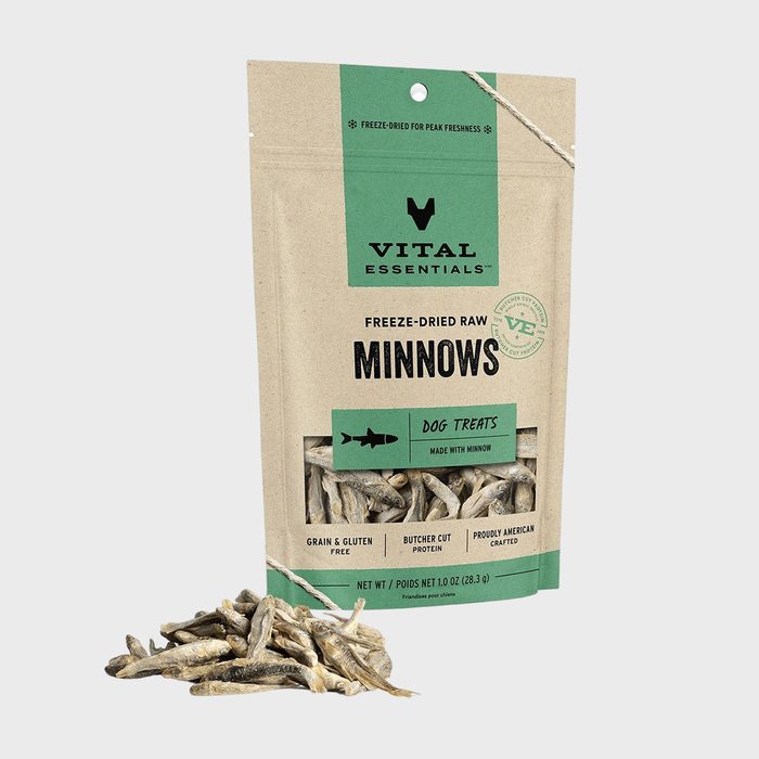 Bag of freeze-dried raw minnow dog treats lies open, spilling contents. The beige packaging features green accents and text emphasizing freshness and quality.
