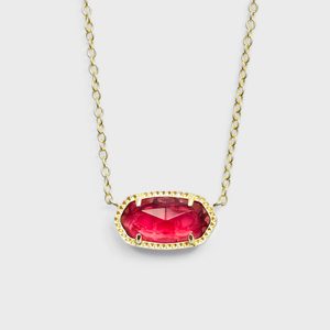 A gold necklace displays a faceted oval red gemstone, suspended on a light gray background.