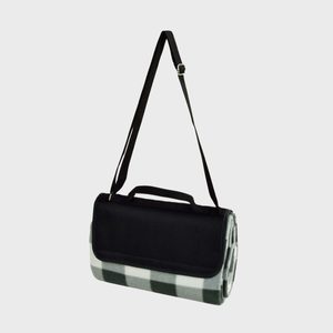 A rolled-up picnic blanket with a black carrying strap hangs against a plain background.