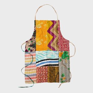Patchwork apron displaying various colorful patterns, hanging against a plain, light background.