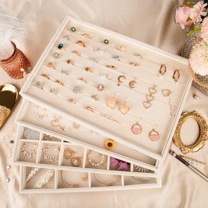 Jewelry trays display earrings, rings, and bracelets, arranged neatly. The scene includes decorative feathers, flowers, and a mirror on a beige fabric surface.