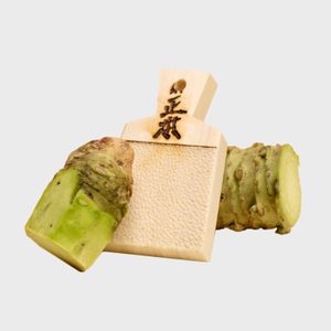 Wasabi root resting on a wooden grater inscribed with Japanese characters; isolated on a plain background.