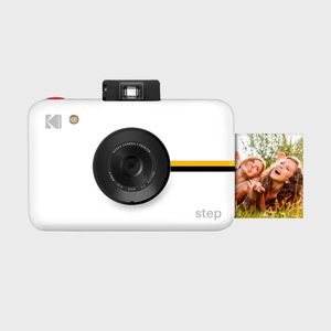 A white instant camera prints a smiling photograph, featuring a yellow stripe. Text reads 