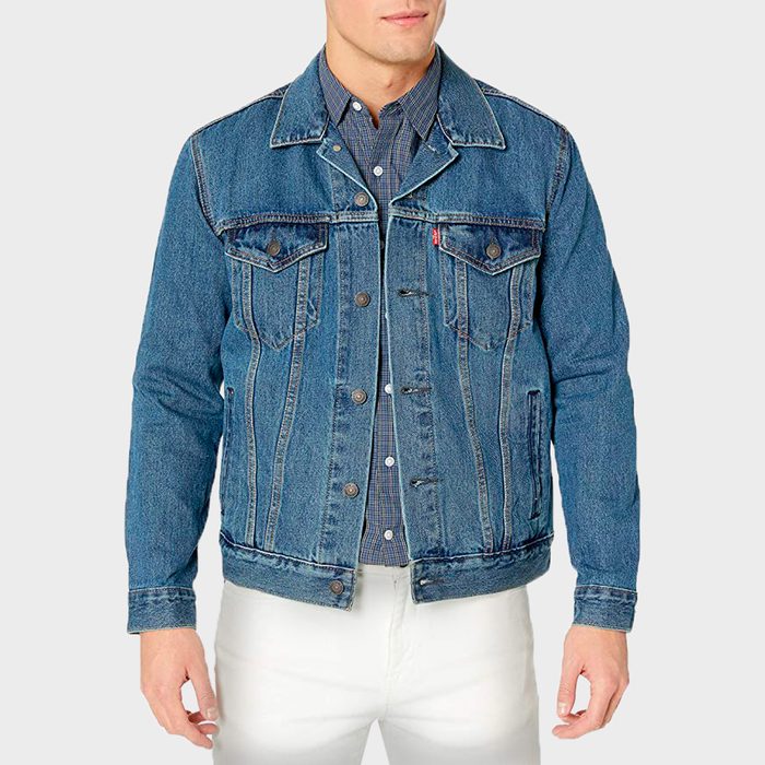 Person wears a blue denim jacket over a checkered shirt, paired with white pants, standing against a plain background.
