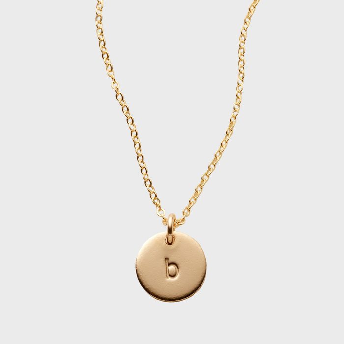 Gold necklace displays a round pendant engraved with the letter 