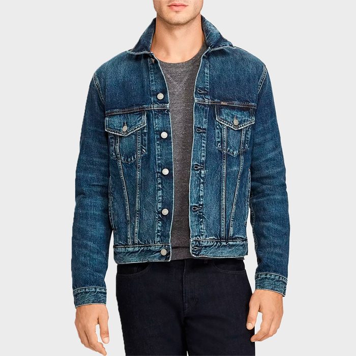 A person wears a blue denim jacket over a gray shirt, standing against a plain light gray background.