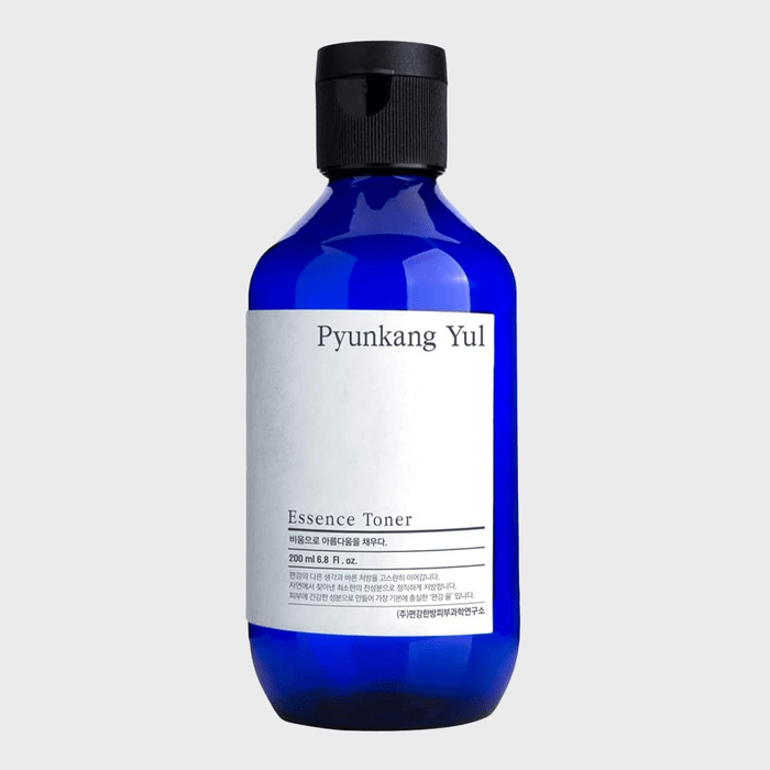 Blue bottle holds Pyunkang Yul Essence Toner, featuring minimalistic white label with text. Bottle stands upright on a plain, light background.