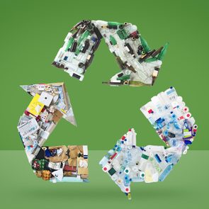 Recycling symbol formed by various recyclables; cardboard, glass, plastic; on a green background.