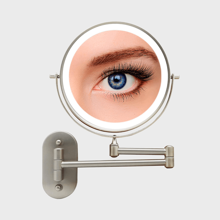 A circular mirror displays a close-up of a blue eye, mounted on a metal adjustable arm against a plain background.