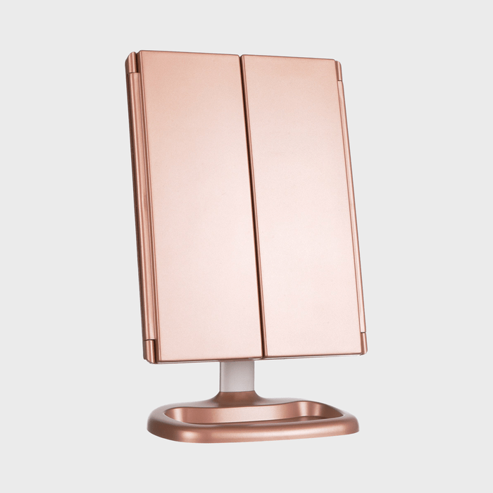 A closed, rose gold folding mirror stands upright on a supportive base against a plain gray background.