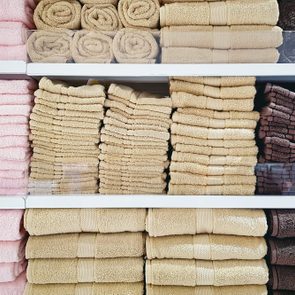 Towels neatly stacked and rolled, displayed in a store on three shelves, arranged by color: pink, beige, and brown.