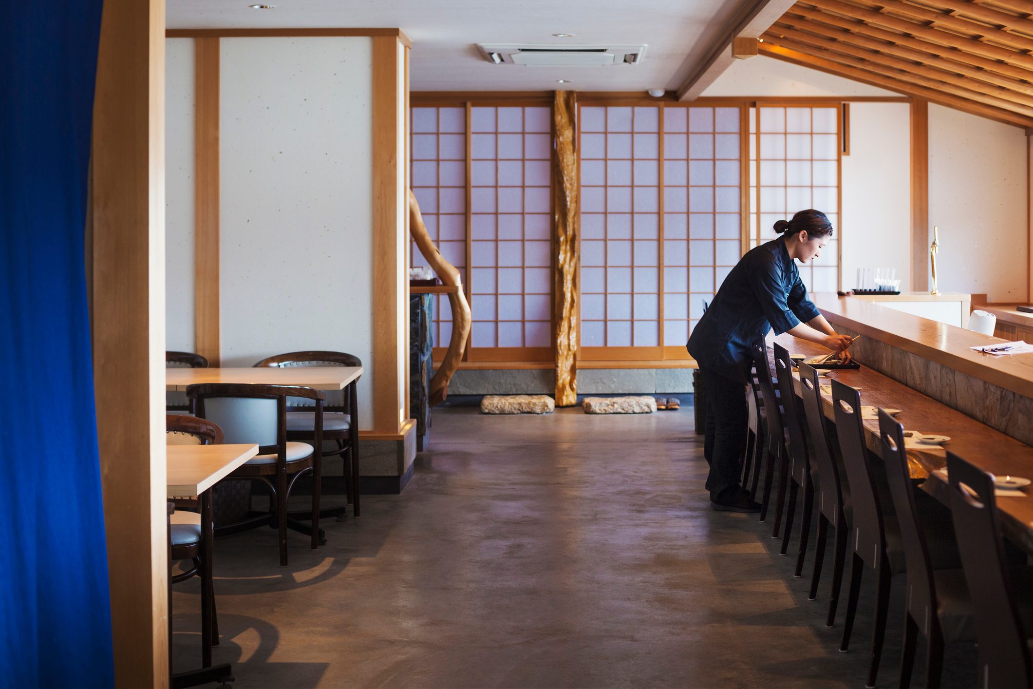 Waitress standing at a counter in a Japanese sushi restaurant, preparing place settings.