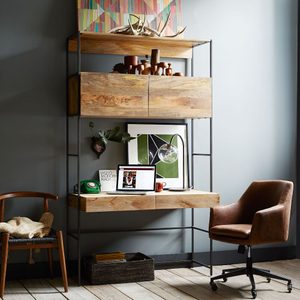 Bookshelf holds wooden decor; a desk displays an open laptop and green phone, surrounded by art, plants, and chairs in a cozy room.