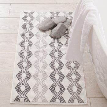 Slippers rest on patterned rug beside white bathtub in a bright, tiled bathroom setting.