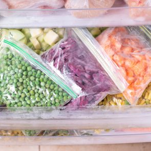 Bags of frozen vegetables arranged inside a freezer drawer, showcasing vibrant green peas, orange carrots, and mixed vegetables.