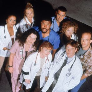 A group of nine medical professionals stand together, looking up, in a hospital setting, some wearing white coats, with stethoscopes visible.