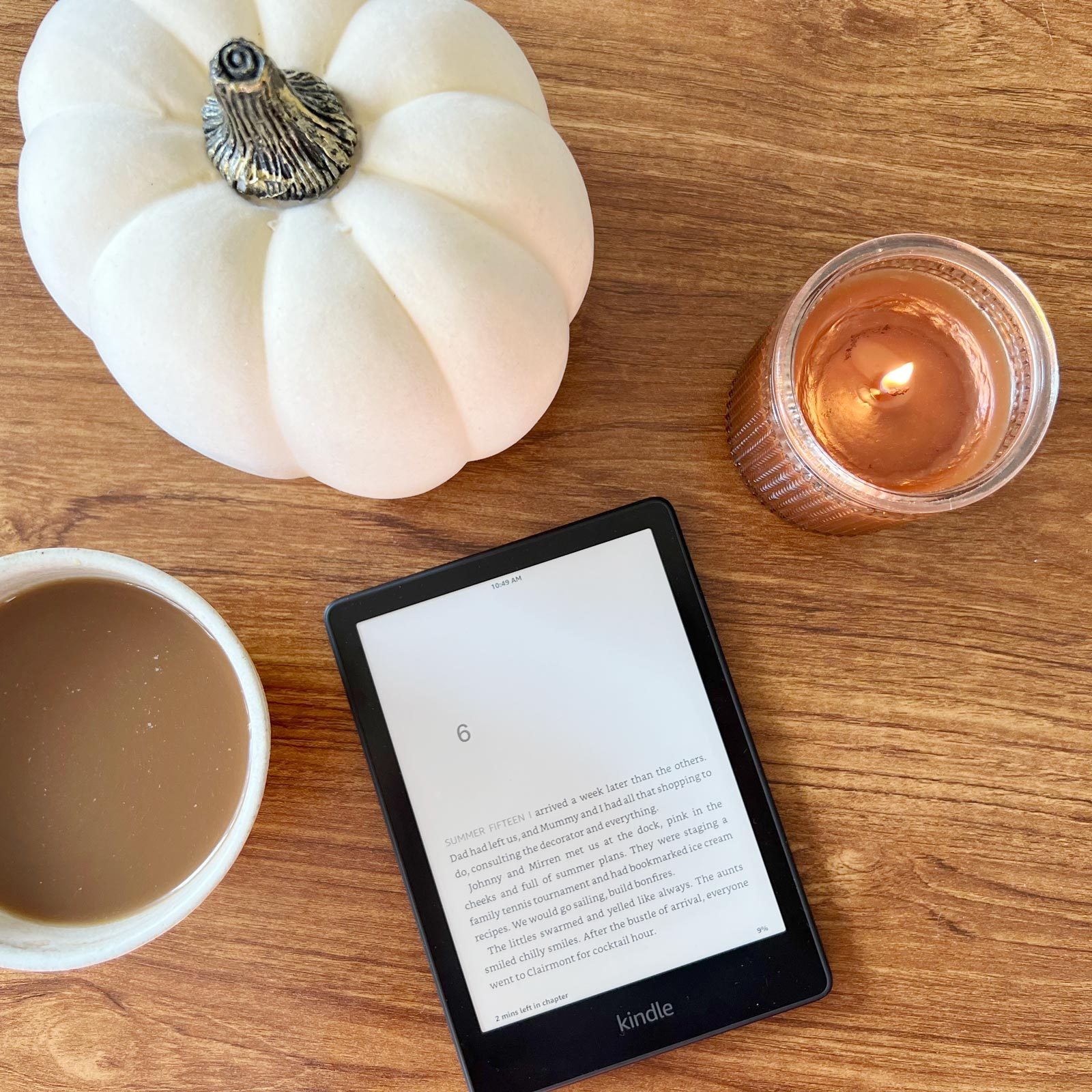 Kindle Paperwhite on a table with a candle, mini white pumpkin and a cup of coffee, viewed from above