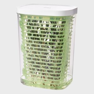 Container holds fresh herbs in a green, slatted structure, enclosed by a transparent exterior and white lid, sitting on a flat surface.