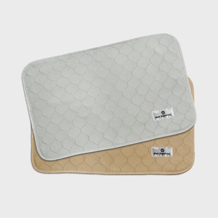 Two quilted pads lie stacked, one gray and one beige, each with a 