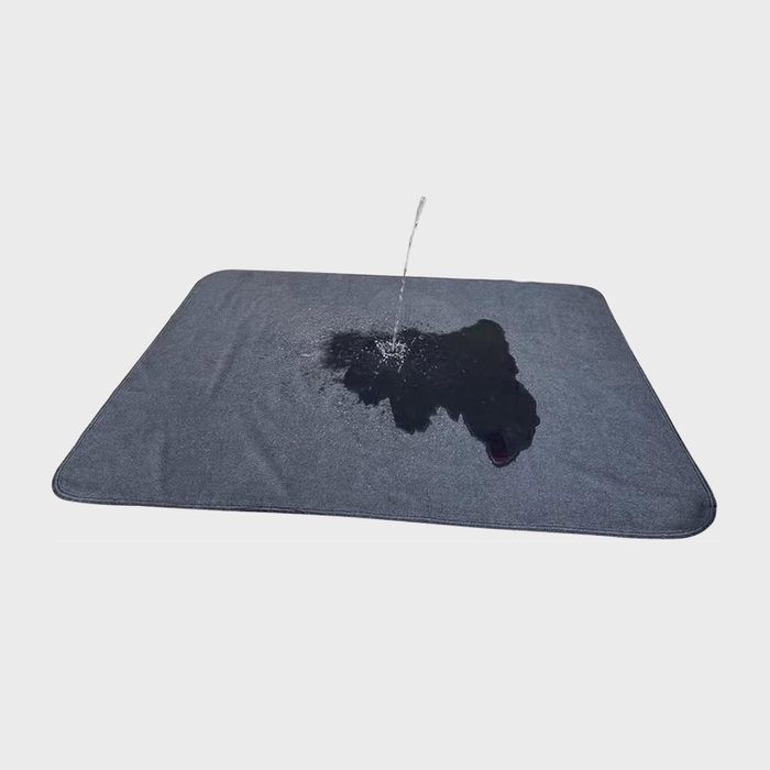 Water splashes onto a dark rectangular mat, creating a wet spot, on a plain white background.