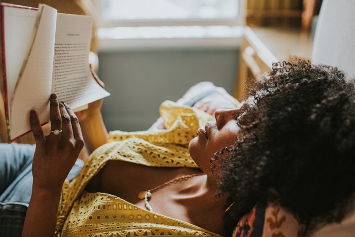 A content woman reclines on a comfortable bed and gets lost in a good book