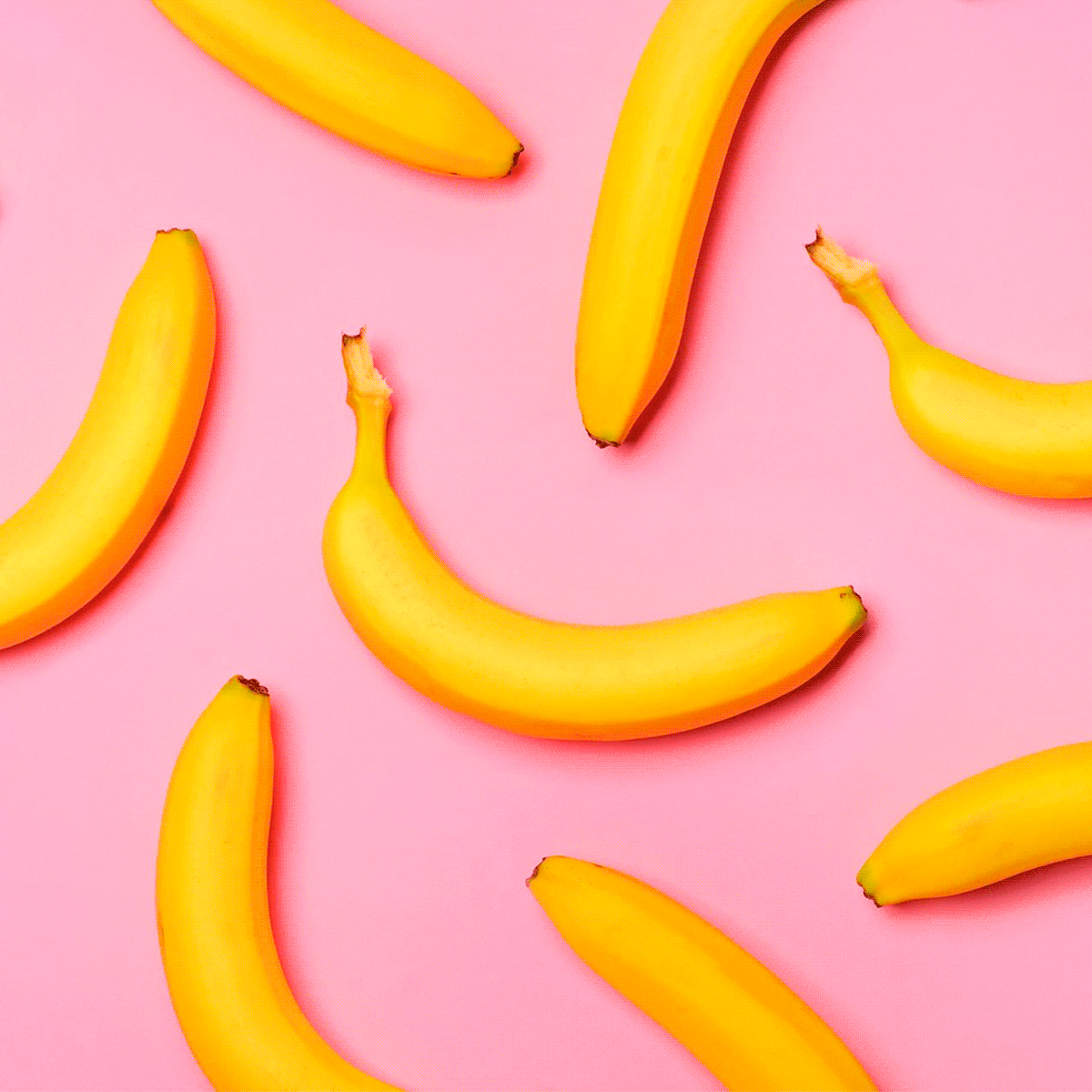 Bananas lie scattered across a pink background, arranged in various angles and positions.