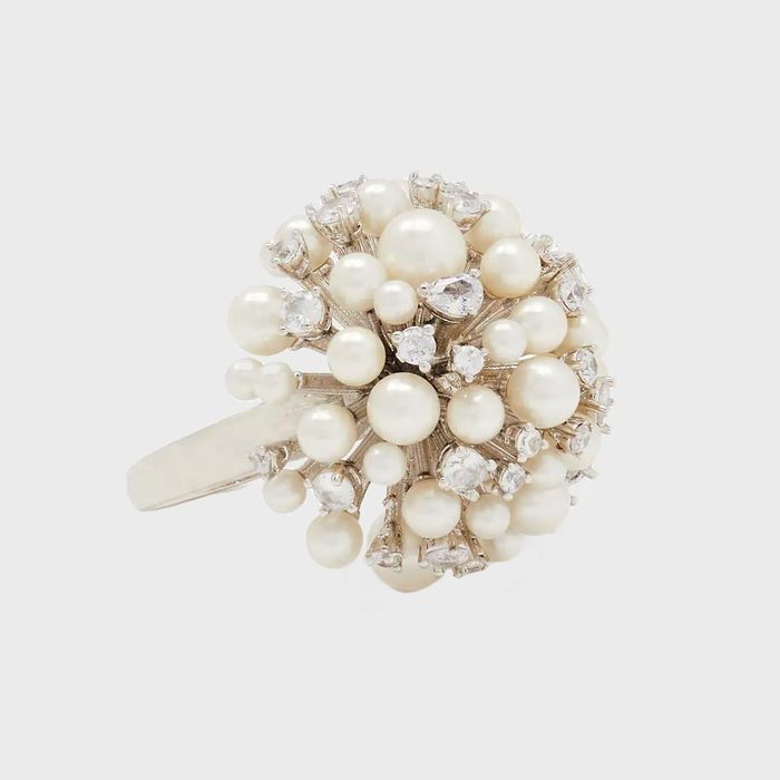 Ring displays clusters of pearls and clear gemstones, resembling a floral bouquet, set against a plain, light gray background.