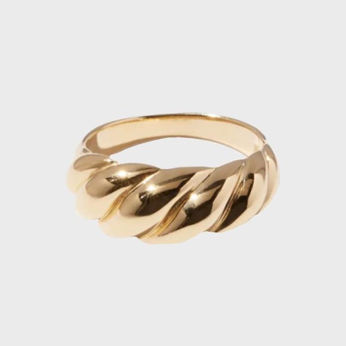 A twisted gold ring rests against a plain, light gray background.