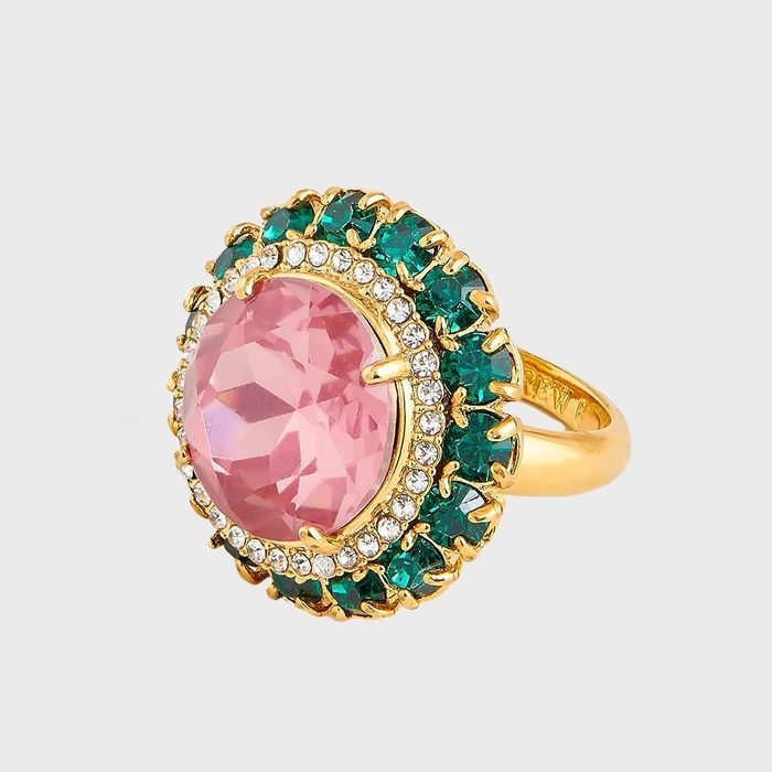 Gold ring displays a large pink gemstone, surrounded by small clear and green stones, on a plain white background.