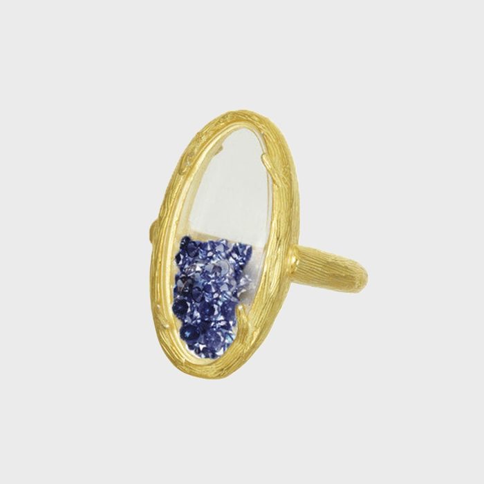 Gold ring encases shifting blue gemstones, creating a dynamic visual set against a plain, light background.